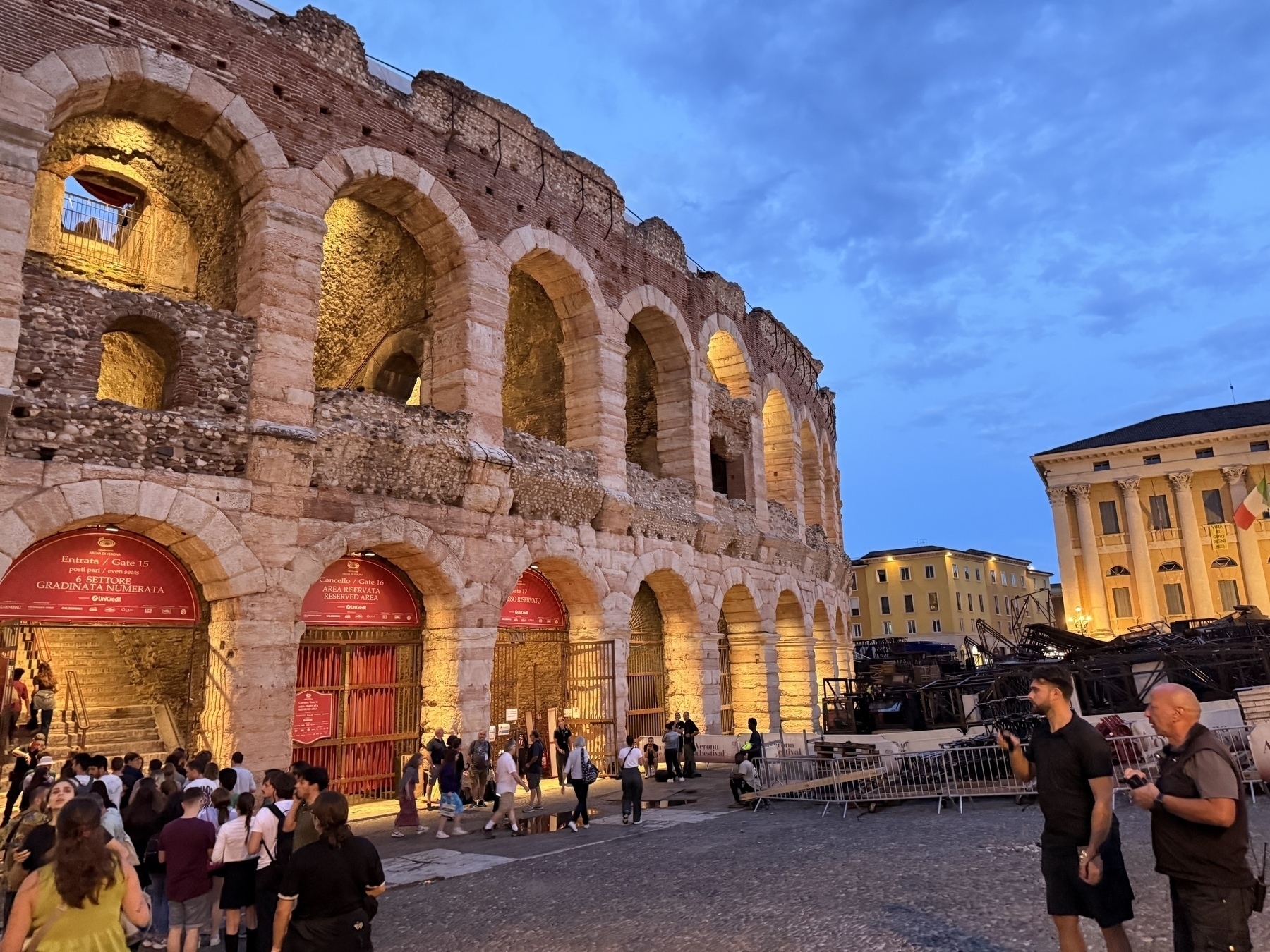 Una folla di persone solleva le mani in aria in un'atmosfera festosa, illuminata da luci rosse.